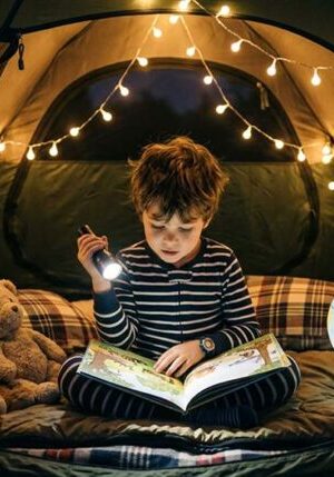 Young boy reading inside a tent decorated with string lights, surrounded by teddy bears and a globe